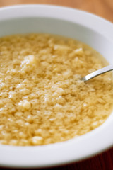 Typical German homemade chicken broth with tiny, Italian star-shaped noodles, called Stelline, in white soup plate with spoon as prevention or remedy when having a cold