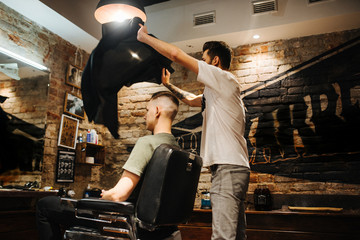 Creating new hair look. Making haircut look perfect. Young bearded man getting haircut by hairdresser while sitting in chair at barbershop