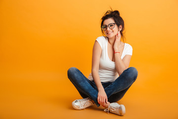Photo of beautiful girl 20s wearing eyeglasses and sneakers sitting with legs crossed on the floor...