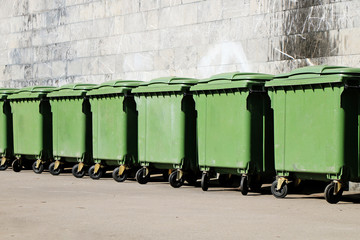 A row of green garbage containers on the city street.