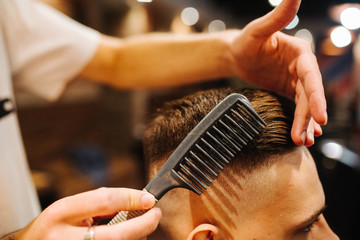 Creating new hair look. Making haircut look perfect. Young bearded man getting haircut by...
