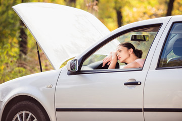 Young woman waits for assistance near her car, which broken down on the road side