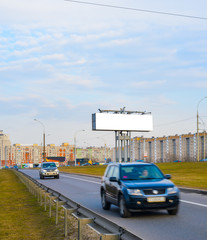 Blank white billboard on the highway with passing cars on the background of multi-storey city buildings, mock up