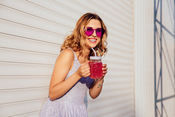 Attractive charming girl in stylish sunglasses, drinking cold beverage, enjoying the summer day, outdoors. Dressed in summer dress. © Maksym Azovtsev