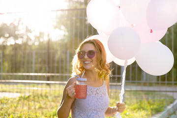 Attractive pretty girl with air balloons drinking a fresh beverage, enjoying the sunny days, while walking outdoors. © Maksym Azovtsev