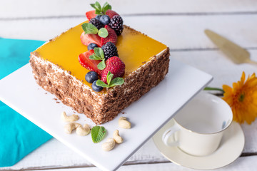 Homemade square cake decorated on top of yellow jelly and berries with mint on light background.