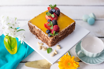 Homemade square cake decorated on top of yellow jelly and berries with mint on light background.