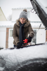 Woman Using Jumper Cables On Car Battery On Snowy Day