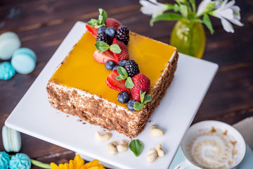 Homemade square cake decorated with yellow jelly on top and berries with mint on dark background