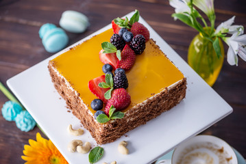 Homemade square cake decorated with yellow jelly on top and berries with mint on dark background