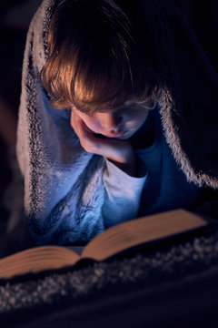 Boy reading book with flashlight