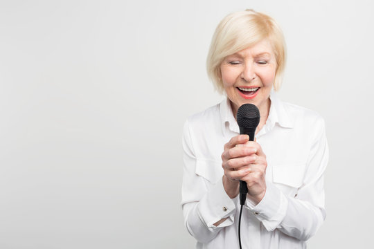 Beautiful and tender picture of awesome mature woman singing a song with her eyes closed using a microphone. Isolated on white background.