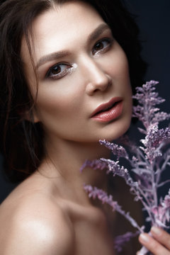 Beautiful woman with a light natural make-up and perfect skin with flowers in her hand. Beauty face. Picture taken in the studio on a black background.