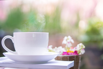 white cup of hot coffee drinking outdoor with some books and nature blur background in morning 