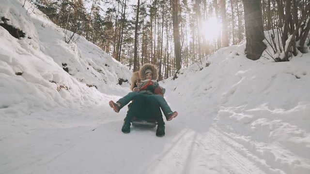 Young mother and little daughter having fun on sledge in winter park in slow motion. Cold snowy weather. Active leisure concept. Steadicam shot