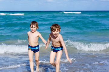 Two kid boys running on ocean beach. Little children having fun