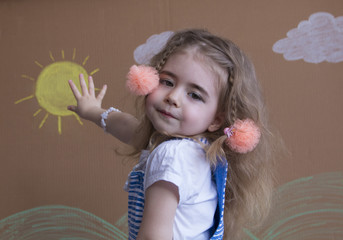 Emotional portrait little girl and pigtails look at the camera. Background of painted sun and white clouds