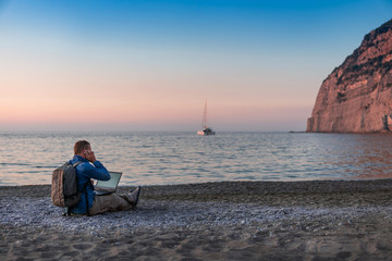 Fototapeta premium young man with laptop working on the beach. Freedom, remote work, freelancer, technology, internet, travel and vacation concepts