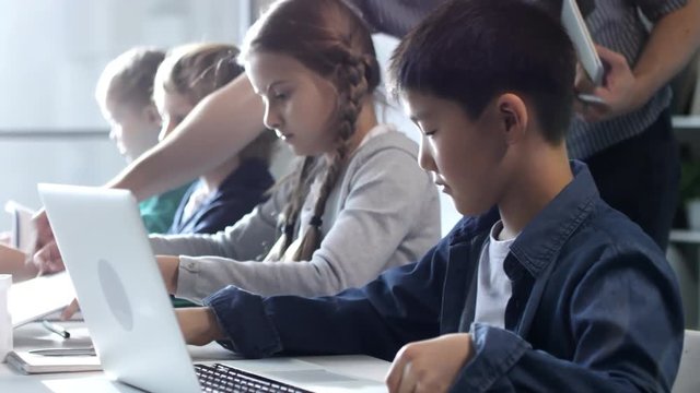 Primary school students sitting in computer coding class and working on their laptop computers under teacher's guidance