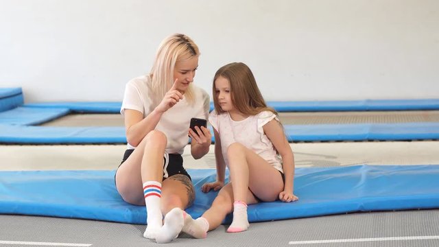 Mother And her daughter sitting on trampoline in fitness park.