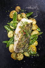 Fried cod fish fillet with vegetable and potatoes as top-view on old board