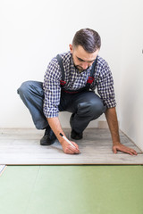 Male worker installing laminate flooring, man installing new wooden laminate flooring. Man laying laminate flooring at home. Carpenter worker installing laminate flooring in the room