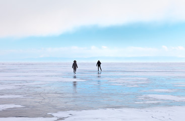 Silhouettes of two girls skating on the ice of the frozen Lake Baikal