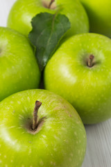 Green apples with leaves on white wooden table Vertical composition