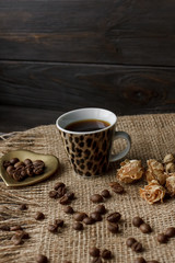 Bronze glass vase with pressed flower on a tablecloth. Golden hearth-shaped saucer with roasted coffee beans. Pure arabica on a wooden table. Lighted candle on the background. Aromatic breakfast