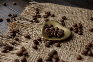 Bronze glass vase with pressed flower on a tablecloth. Golden hearth-shaped saucer with roasted coffee beans. Pure arabica on a wooden table. Lighted candle on the background. Aromatic breakfast