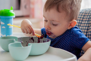 Little toddler boy with dirty face eating fresh blueberry indoor