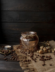 Vase with pressed flower on a tablecloth. Golden hearth-shaped saucer with roasted coffee beans. Pure arabica on a wooden table. Lighted candle on the background. Aromatic breakfast