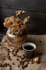 Vase with pressed flower on a tablecloth. Golden hearth-shaped saucer with roasted coffee beans. Pure arabica on a wooden table. Lighted candle on the background. Aromatic breakfast