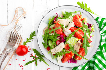 Chicken fillet salad with tomato, lettuce, cucumber and arugula leaves. Fresh vegetable salad with chicken meat. Healthy food. White wooden background. Top view
