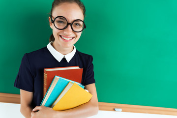 Happy joyful student likes read a books. Photo of young girl hugging books near blackboard, creative concept with Back to school theme