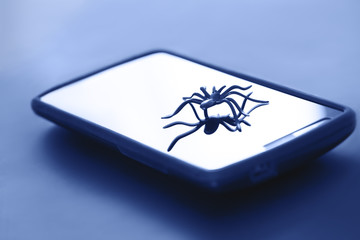 Cute spider toy posing on surface of gadget display. Plastic spider toy in action on surface of device screen. Best picture for web, digital communication & mobile technology concept.