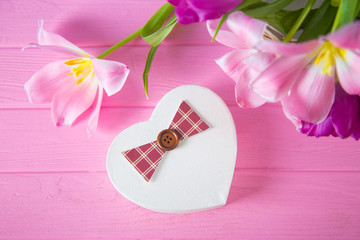 Gift box in shape of heart and tender bouquet of beautiful pink tulips on pink wooden background