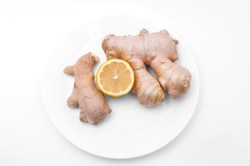 On a white background a plate of ginger and a half of fresh lemon.