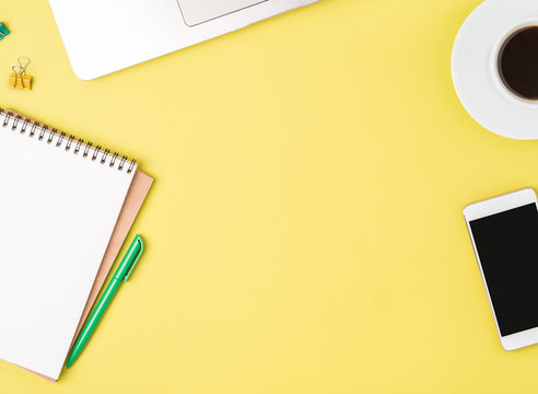 Top View Of Modern Bright Yellow Office Desktop With Blank Notepad, Computer, Smartphone. Mock Up, Empty Space