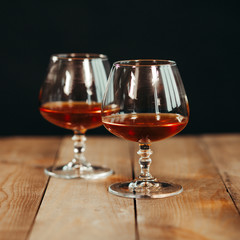 Close up of two glass goblets with alcohol resting on a wooden table against a dark background