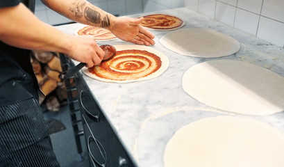 cook applying tomato sauce to pizza at pizzeria
