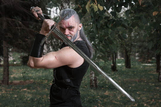 сosplay, Dressed Like A Hero Geralt Of Rivia From The Game The Witcher, A Fantastic Warrior With A Sword In His Hands