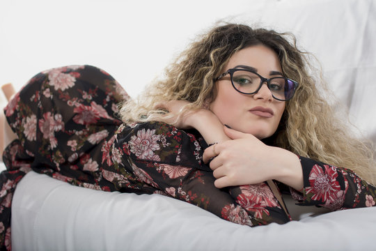 Woman with curly hair and floral dress posing on bed