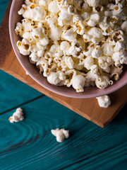 Popcorn in pink bowl on wooden board on dark green background