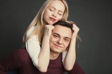 Portrait of a beautiful young couple in love posing at studio over dark background. Girl sitting on the shoulders of a young man and holds him by the hair