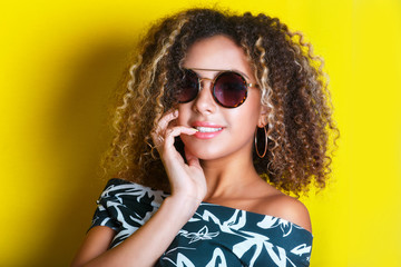 Beauty portrait of young african american girl with afro hairstyle. Girl posing on yellow background, looking at camera. Studio shot.