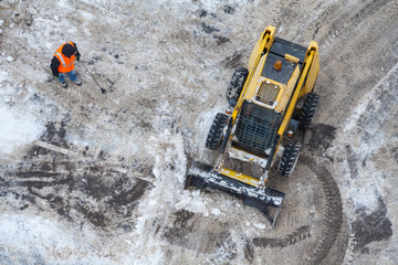 Top view of a snow-removing machine and worker in orange uniform on a dirty road