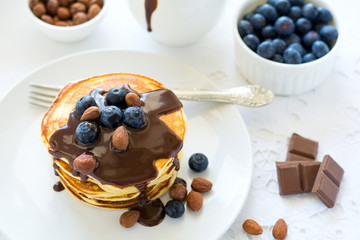 Traditional breakfast concept. Stack of pancakes with chocolate souce, blueberries and nuts on white table cloth. Selective focus