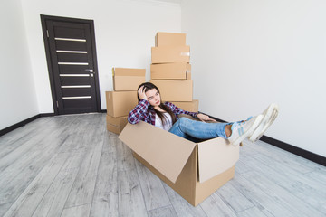 Cheerful sad and tired woman sitting in a cardboard box white moving in new appartmant