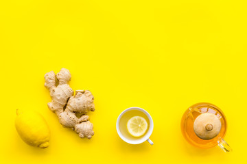 Warming tea with lemon and ginger. Cup, teapot, ginger root on yellow background top view copy space